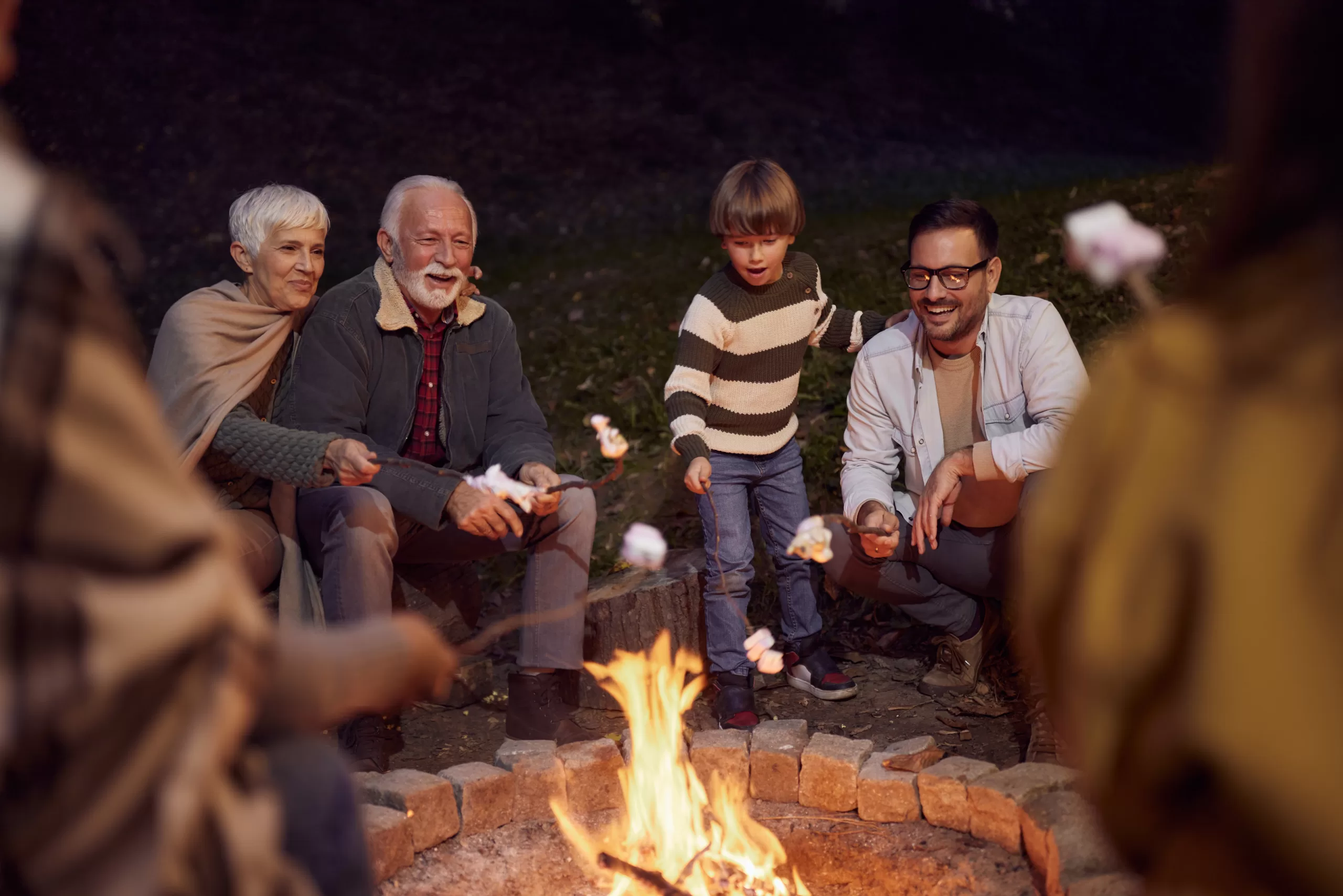 Happy extended family enjoying while roasting marshmallows on fire in the backyard.