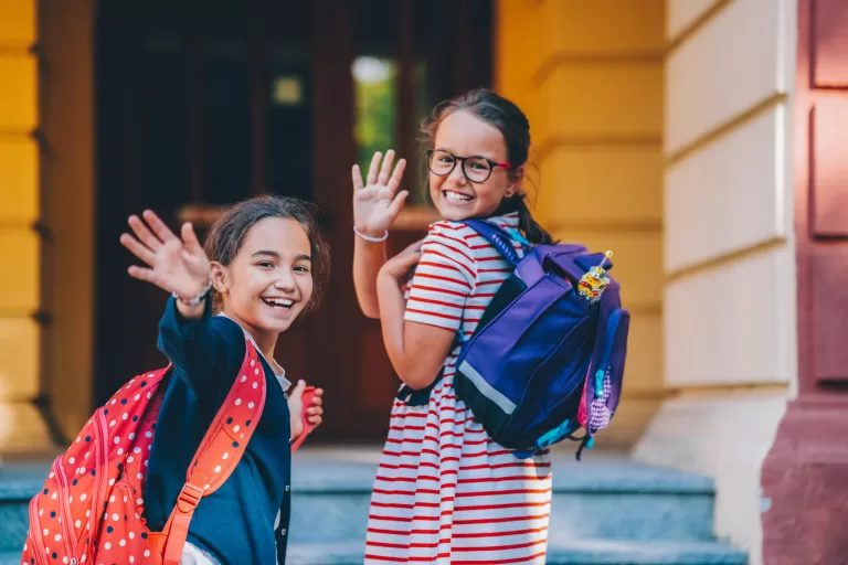 Cute schoolgirls smiling before entering the school building